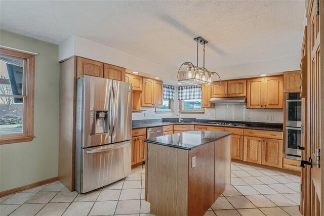 kitchen with light tile patterned floors, a sink, dark countertops, stainless steel appliances, and under cabinet range hood