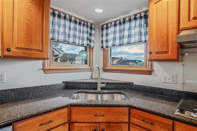 kitchen featuring dark stone counters, recessed lighting, brown cabinets, and a sink