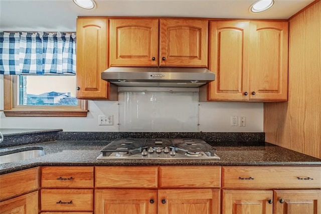 kitchen with dark stone countertops, recessed lighting, stainless steel gas stovetop, under cabinet range hood, and a sink