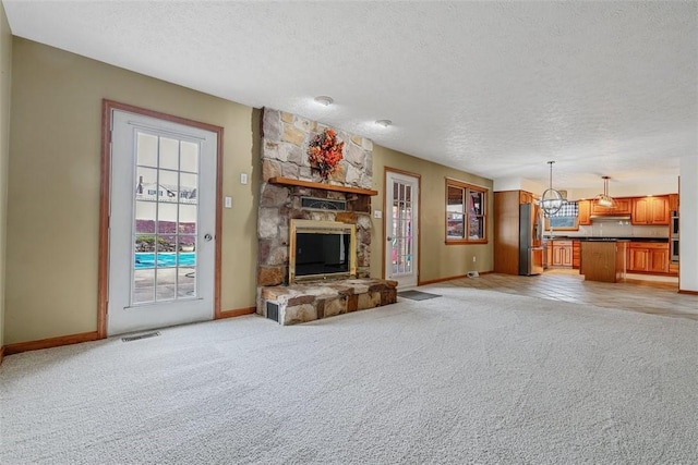 unfurnished living room with a textured ceiling, visible vents, light colored carpet, and a fireplace
