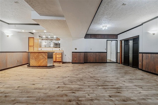 interior space featuring light wood-type flooring, light countertops, a textured ceiling, wainscoting, and open floor plan