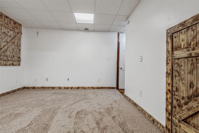 finished below grade area featuring a paneled ceiling, carpet flooring, and baseboards