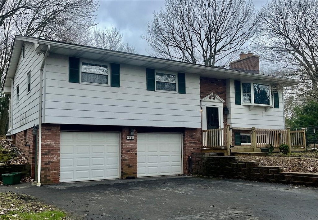 bi-level home with a chimney, brick siding, aphalt driveway, and an attached garage
