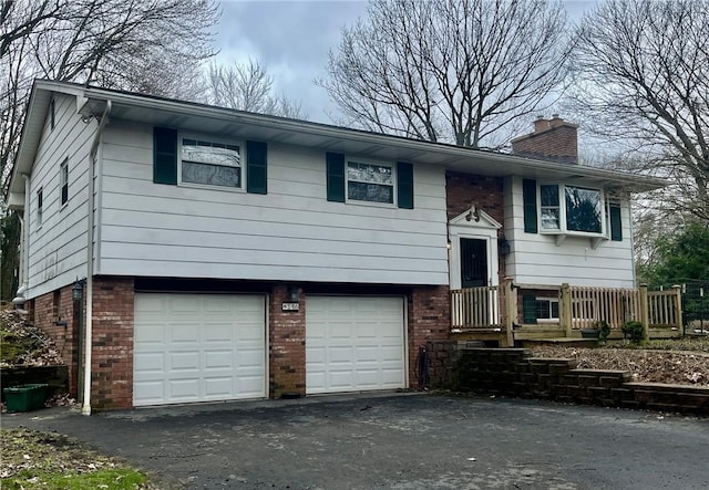 bi-level home with a chimney, brick siding, aphalt driveway, and an attached garage