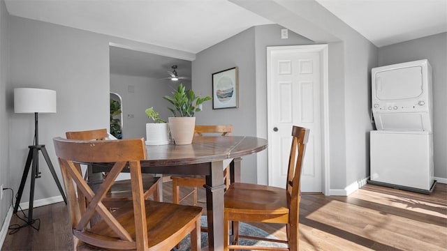 dining room featuring stacked washing maching and dryer, wood finished floors, ceiling fan, and baseboards