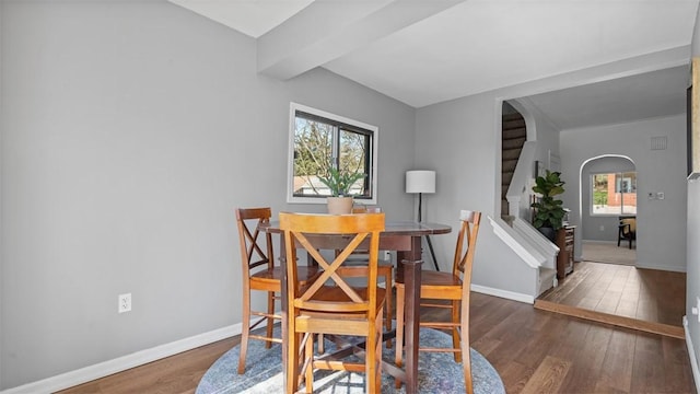 dining room with stairway, wood finished floors, arched walkways, and baseboards