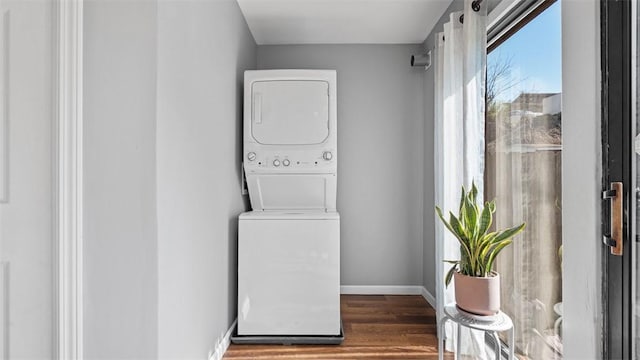 laundry area with stacked washer and dryer, laundry area, wood finished floors, and baseboards