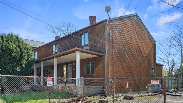 view of home's exterior featuring a chimney, a porch, and a fenced front yard