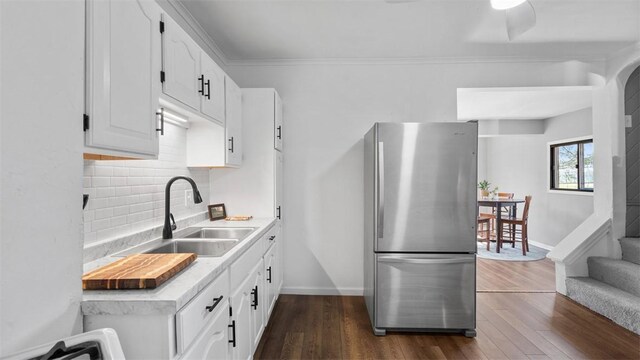 kitchen with tasteful backsplash, a sink, freestanding refrigerator, baseboards, and dark wood-type flooring