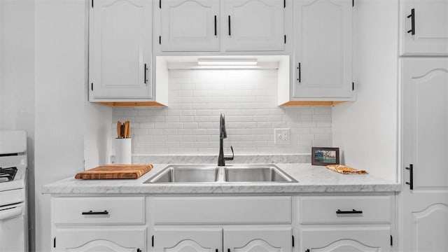 kitchen with white range with gas cooktop, a sink, backsplash, and white cabinetry