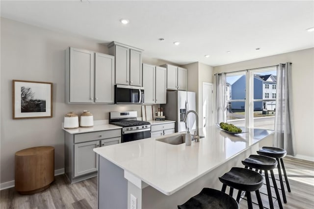 kitchen featuring appliances with stainless steel finishes, a sink, light wood-style flooring, and gray cabinets