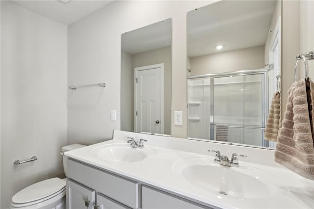 bathroom with toilet, double vanity, a sink, and a shower stall
