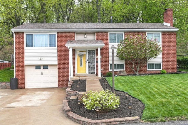 raised ranch with concrete driveway, a chimney, brick siding, a front lawn, and a garage