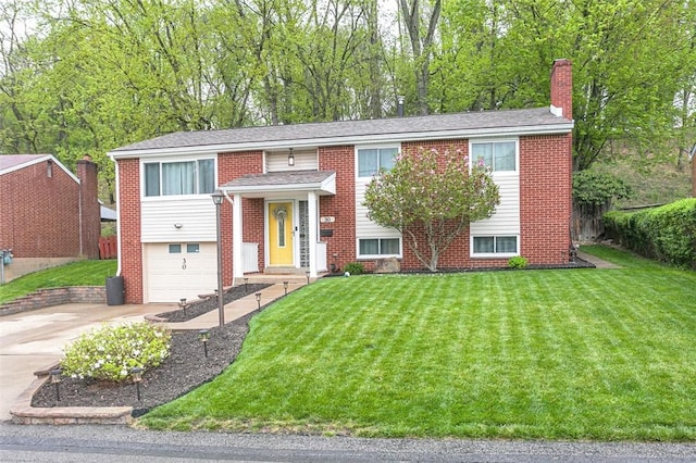 raised ranch with a chimney, brick siding, driveway, a front yard, and an attached garage