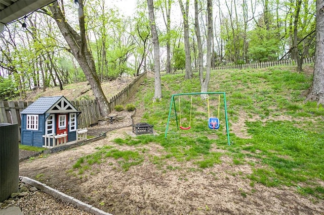 view of yard with an outdoor fire pit, a fenced backyard, an outbuilding, and a playground