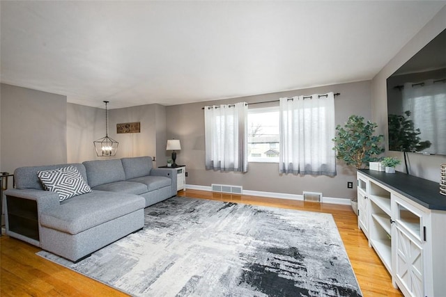 living area with baseboards, visible vents, a notable chandelier, and light wood finished floors