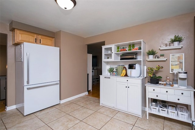 kitchen featuring light countertops, light tile patterned flooring, open shelves, baseboards, and freestanding refrigerator