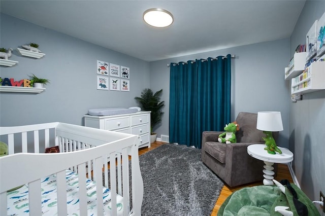 bedroom with wood finished floors, baseboards, visible vents, and a crib