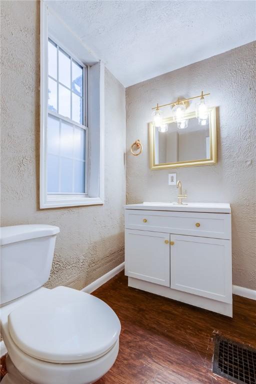 half bathroom with wood finished floors, a textured wall, toilet, and baseboards
