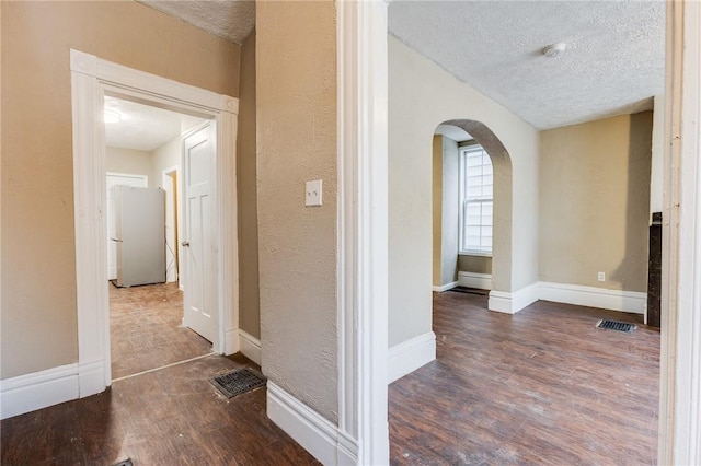 hallway with visible vents, a textured wall, a textured ceiling, arched walkways, and wood finished floors
