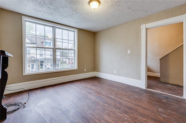 interior space with a textured ceiling, a textured wall, wood finished floors, and baseboards