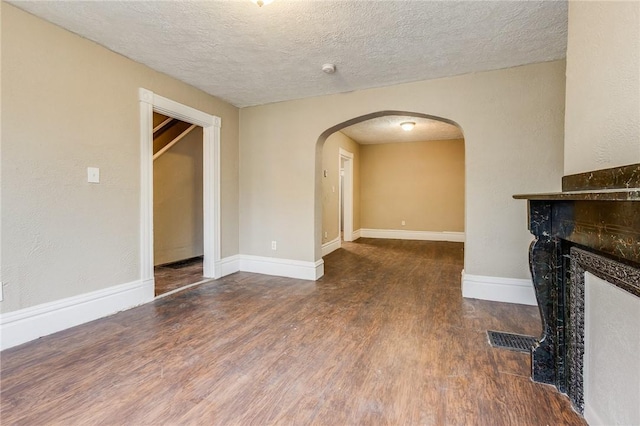 unfurnished living room with a tile fireplace, visible vents, a textured ceiling, arched walkways, and wood finished floors