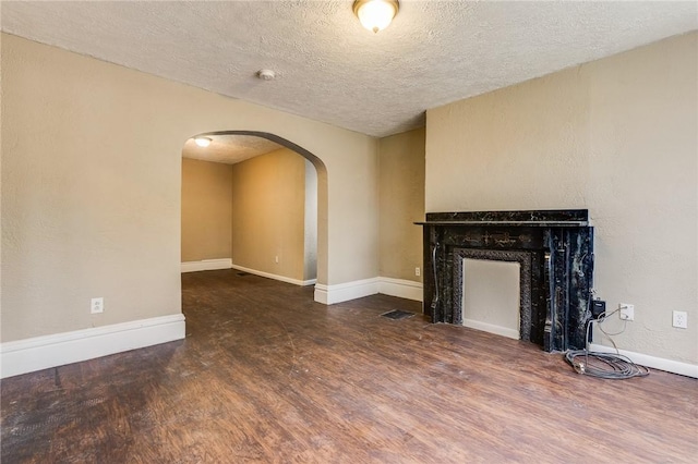 unfurnished living room featuring a textured ceiling, wood finished floors, visible vents, and arched walkways