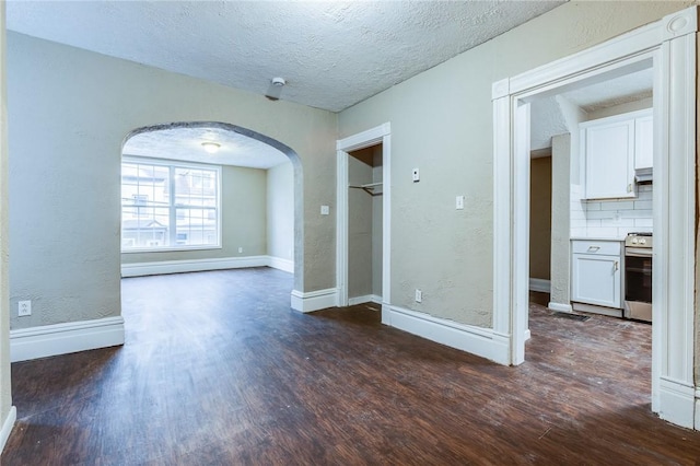 spare room featuring arched walkways, baseboards, a textured ceiling, and dark wood finished floors