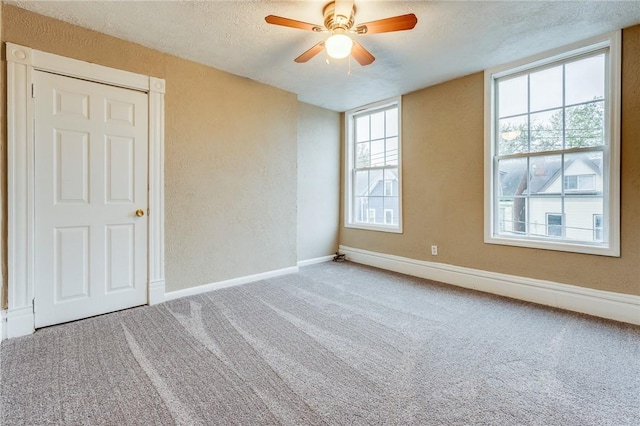 carpeted empty room featuring a textured ceiling, a textured wall, a ceiling fan, and baseboards