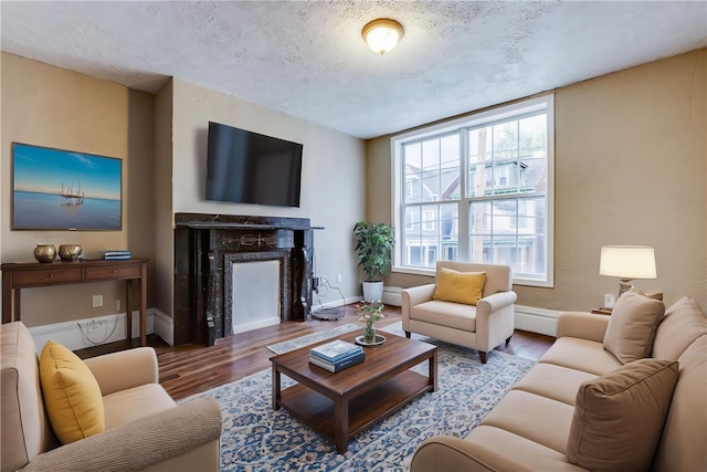 living room featuring a fireplace, a textured ceiling, wood finished floors, and baseboards