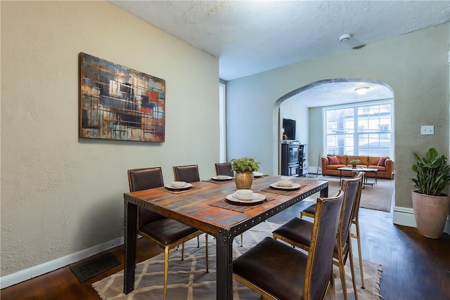 dining area with wood finished floors, baseboards, a textured wall, and arched walkways