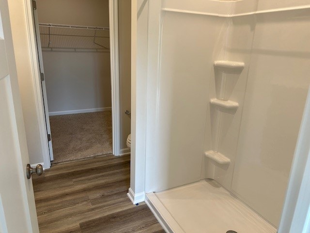 bathroom featuring a walk in closet, a shower stall, wood finished floors, baseboards, and toilet