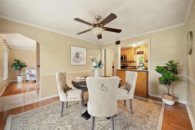 dining room with crown molding, light wood-style floors, ceiling fan, baseboards, and arched walkways