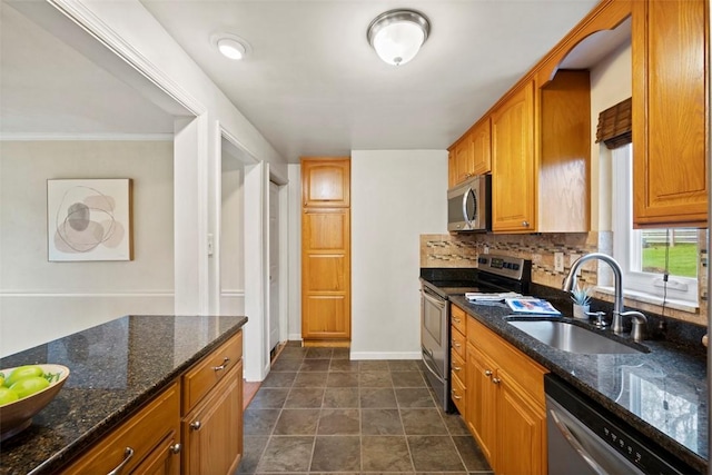 kitchen featuring dark stone counters, a sink, brown cabinetry, tasteful backsplash, and appliances with stainless steel finishes