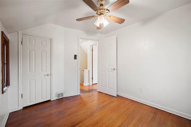 unfurnished bedroom featuring ceiling fan, visible vents, vaulted ceiling, baseboards, and wood finished floors