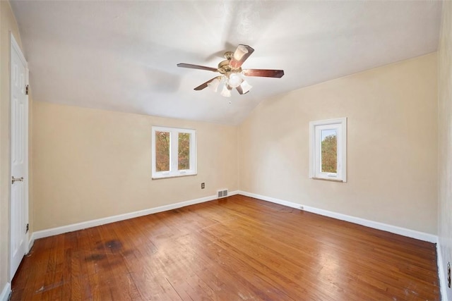 empty room with vaulted ceiling, wood-type flooring, baseboards, visible vents, and a ceiling fan