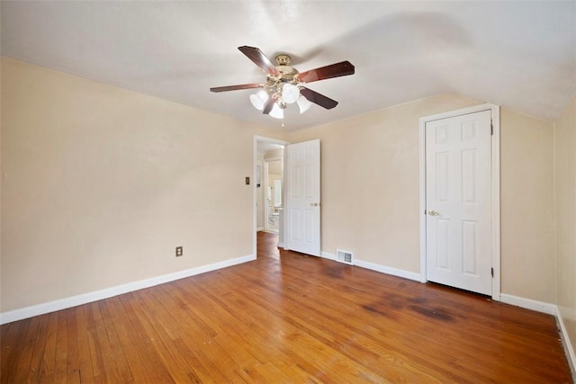 spare room featuring lofted ceiling, hardwood / wood-style flooring, visible vents, baseboards, and a ceiling fan