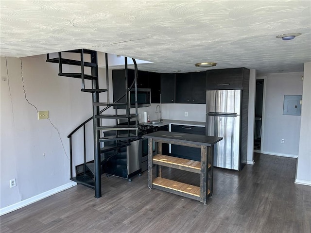 kitchen with stainless steel appliances, electric panel, dark wood-style floors, baseboards, and dark cabinetry
