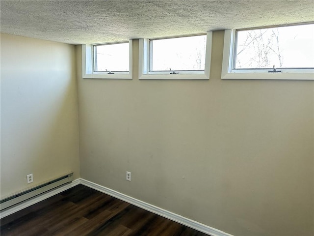 basement with a textured ceiling, a healthy amount of sunlight, dark wood-style floors, a baseboard heating unit, and baseboards