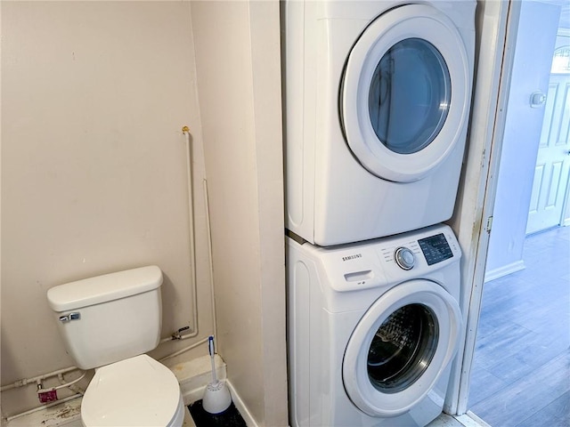 clothes washing area with baseboards, wood finished floors, and stacked washer / drying machine