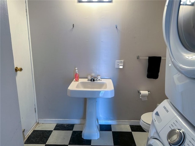 half bath featuring tile patterned floors, stacked washer and clothes dryer, toilet, and baseboards