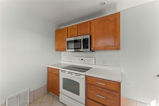 kitchen with stainless steel microwave, light tile patterned floors, visible vents, light countertops, and white range with electric cooktop