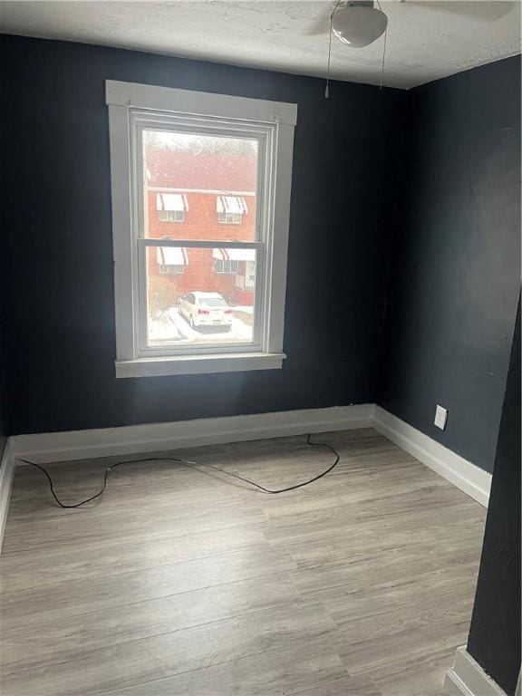 spare room featuring baseboards, a textured ceiling, and light wood finished floors