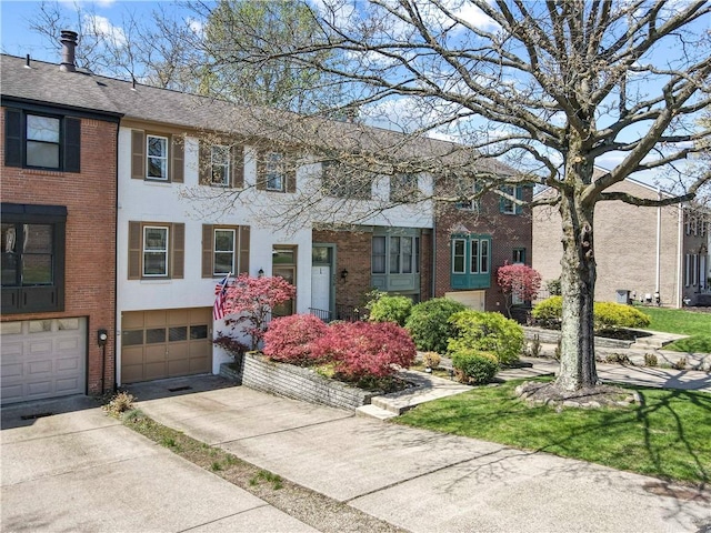 view of property featuring driveway, roof with shingles, brick siding, and a garage