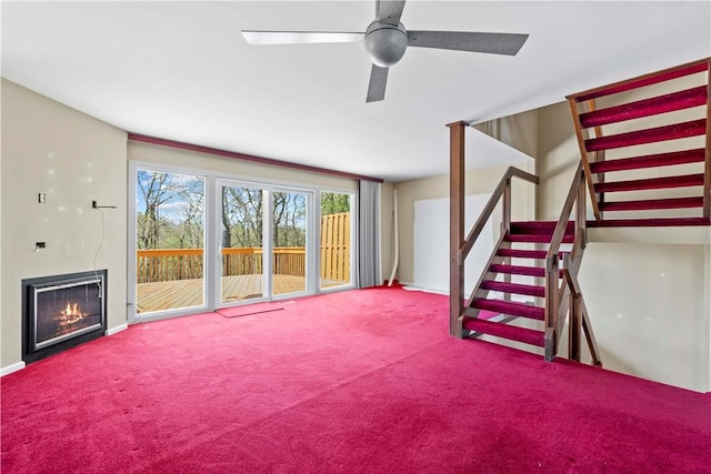 unfurnished living room with baseboards, carpet flooring, stairway, and a warm lit fireplace