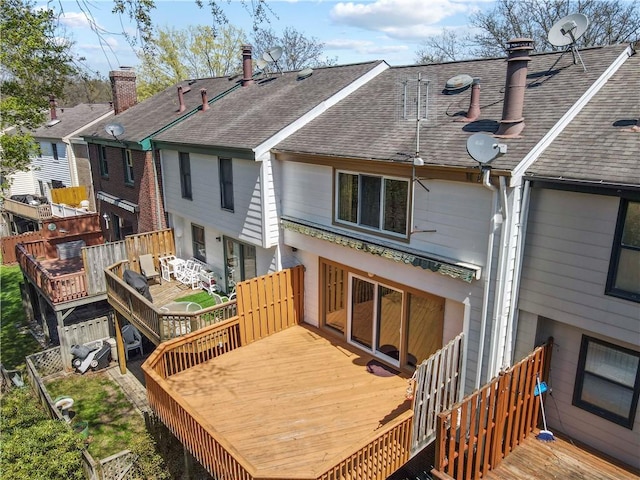 rear view of house featuring a wooden deck, a chimney, and roof with shingles