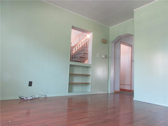 unfurnished room featuring built in features, crown molding, baseboards, arched walkways, and wood finished floors