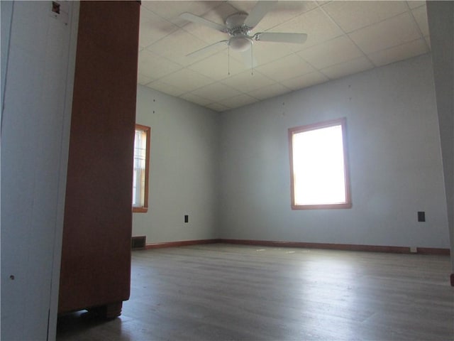 empty room featuring wood finished floors, a drop ceiling, baseboards, visible vents, and a ceiling fan