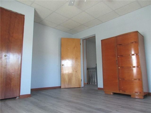 unfurnished bedroom featuring a paneled ceiling, ceiling fan, wood finished floors, and baseboards