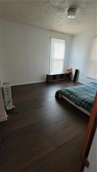 bedroom with a textured ceiling, dark wood finished floors, and baseboards